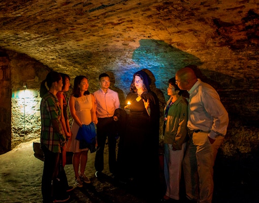Group on Edinburgh ghost tour in underground vaults with guide holding candle.