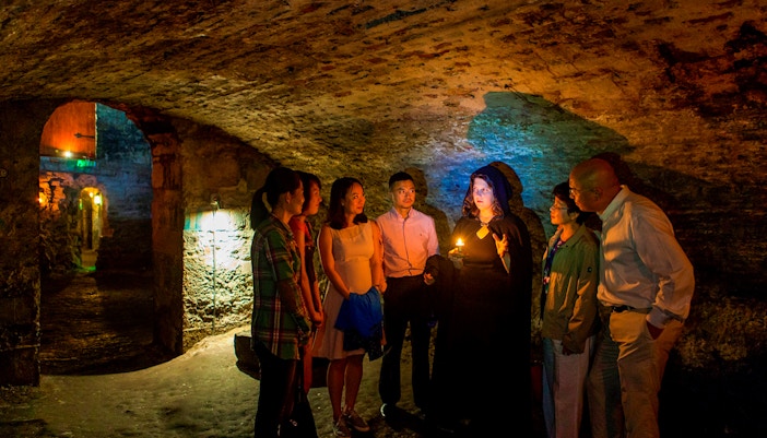 Group on Edinburgh ghost tour in underground vaults with guide holding candle.