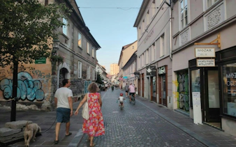 Ljubljana street with people walking and cycling, featuring local shops and graffiti.