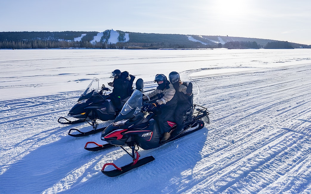 Snowmobilers on frozen lake in Lapland during winter.