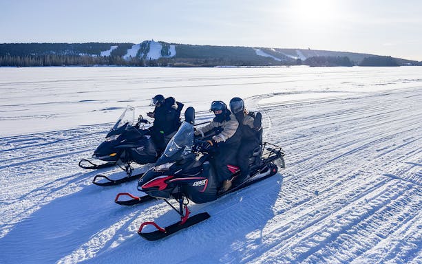 Snowmobilers on frozen lake in Lapland during winter.