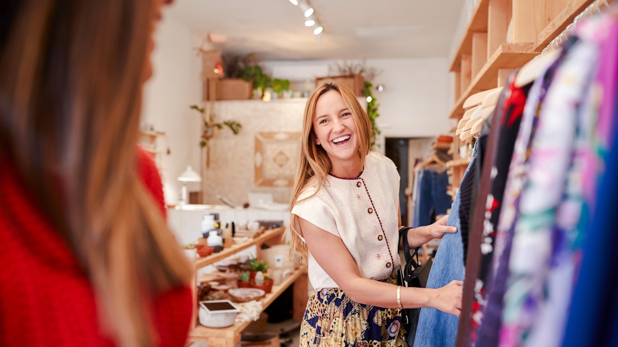 Two women shopping in a boutique, browsing clothes on a rack.