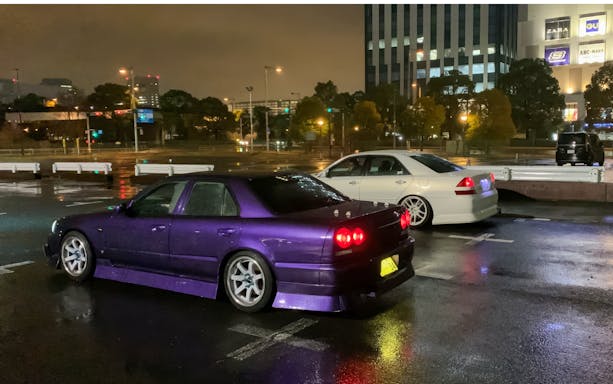 Super cars parked on a rainy street in Tokyo at night.