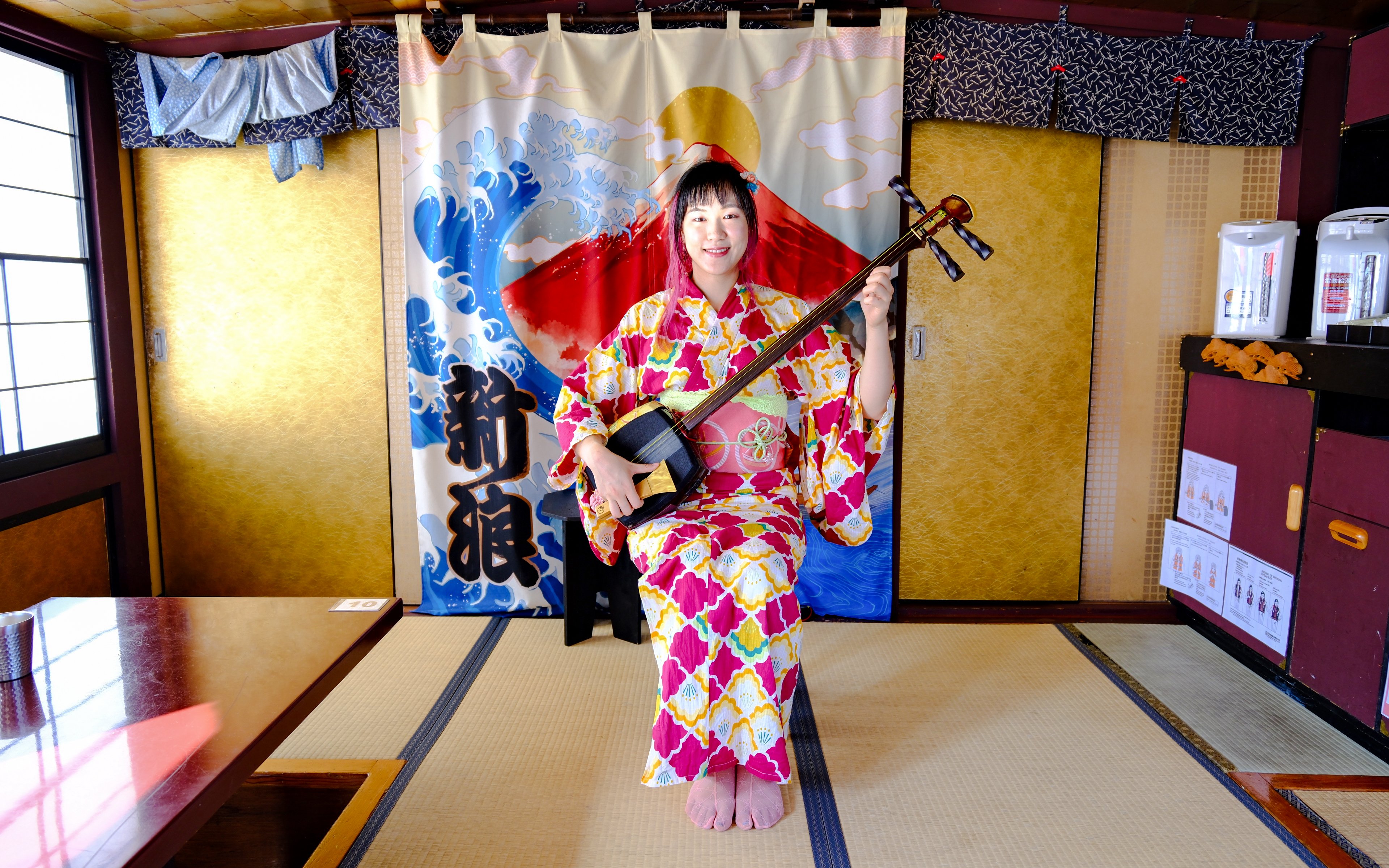 Person in kimono playing shamisen in traditional Tokyo setting.