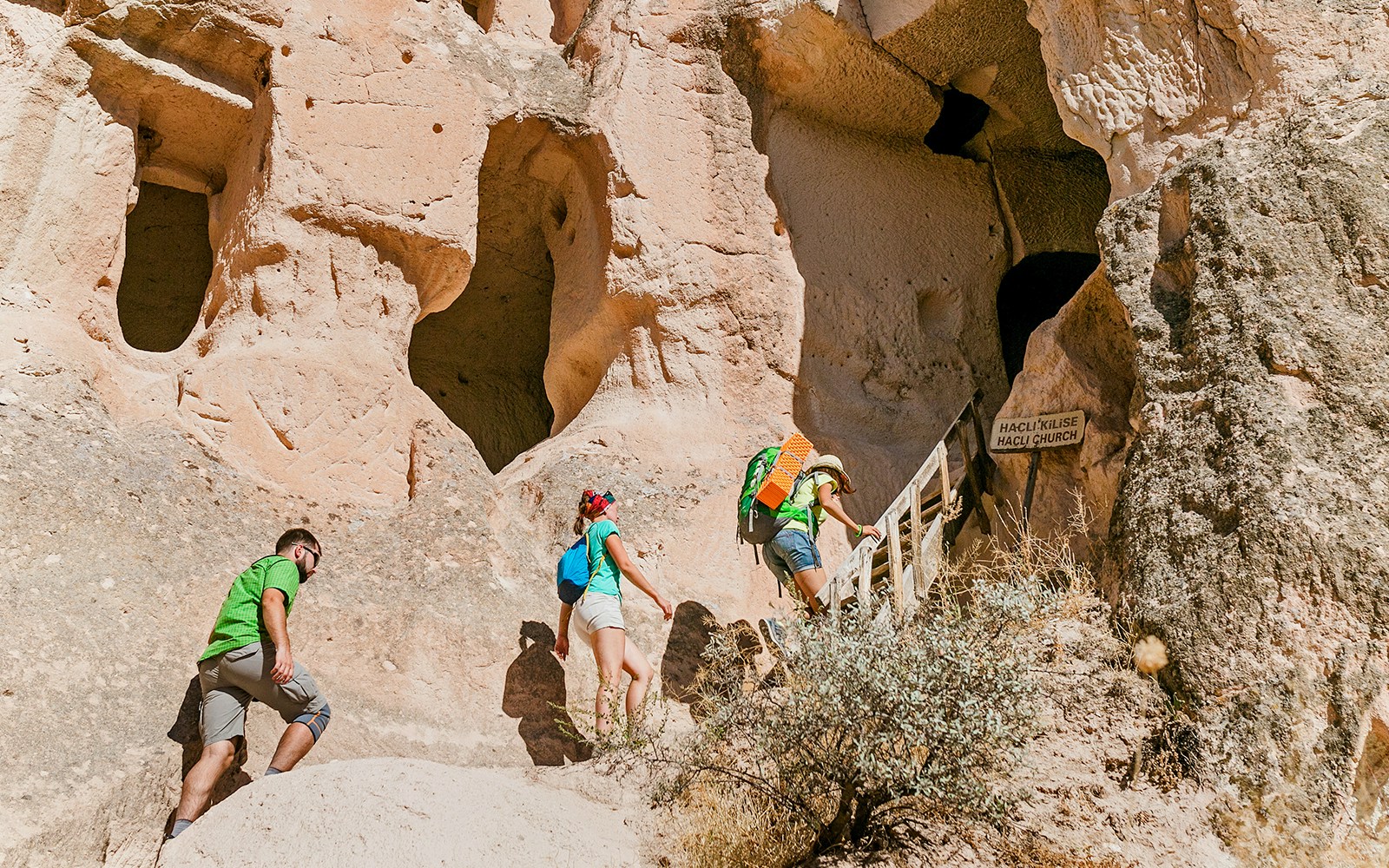 Visitors climbing stairs to ancient church entrance in Cappadocia rock formations.