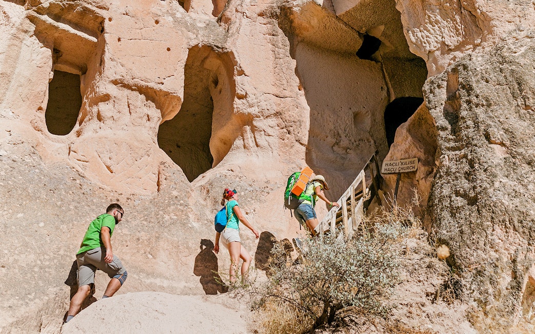 Visitors climbing stairs to ancient church entrance in Cappadocia rock formations.