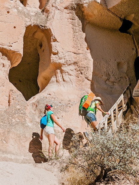 Visitors climbing stairs to ancient church entrance in Cappadocia rock formations.
