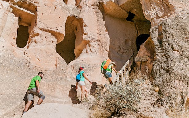 Visitors climbing stairs to ancient church entrance in Cappadocia rock formations.