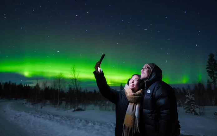 Couple taking selfies under Northern Lights in Levi, Finland.