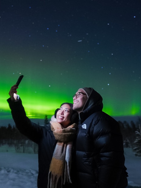 Couple taking selfies under Northern Lights in Levi, Finland.