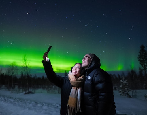 Couple taking selfies under Northern Lights in Levi, Finland.