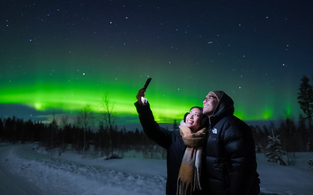 Couple taking selfies under Northern Lights in Levi, Finland.