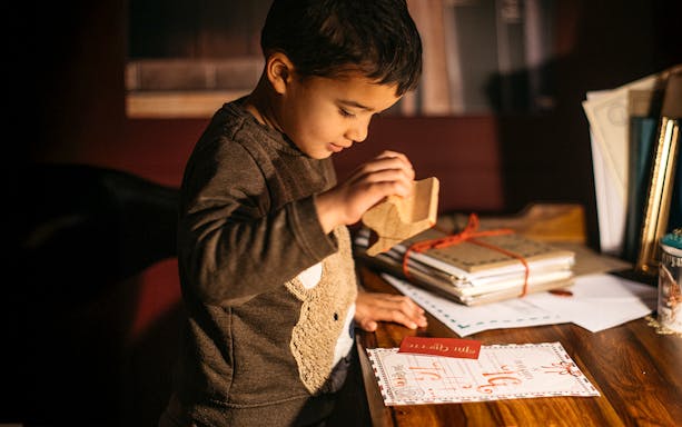Child stamping a letter to Santa at a wooden desk.