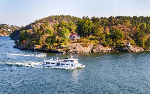 Cruise ship passing by a scenic island with a red house during an archipelago sightseeing tour.
