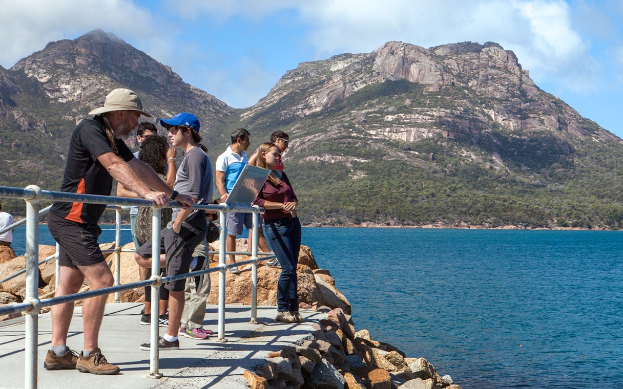 Visitors enjoying the view of Wineglass Bay with mountains in the background, Tasmania.