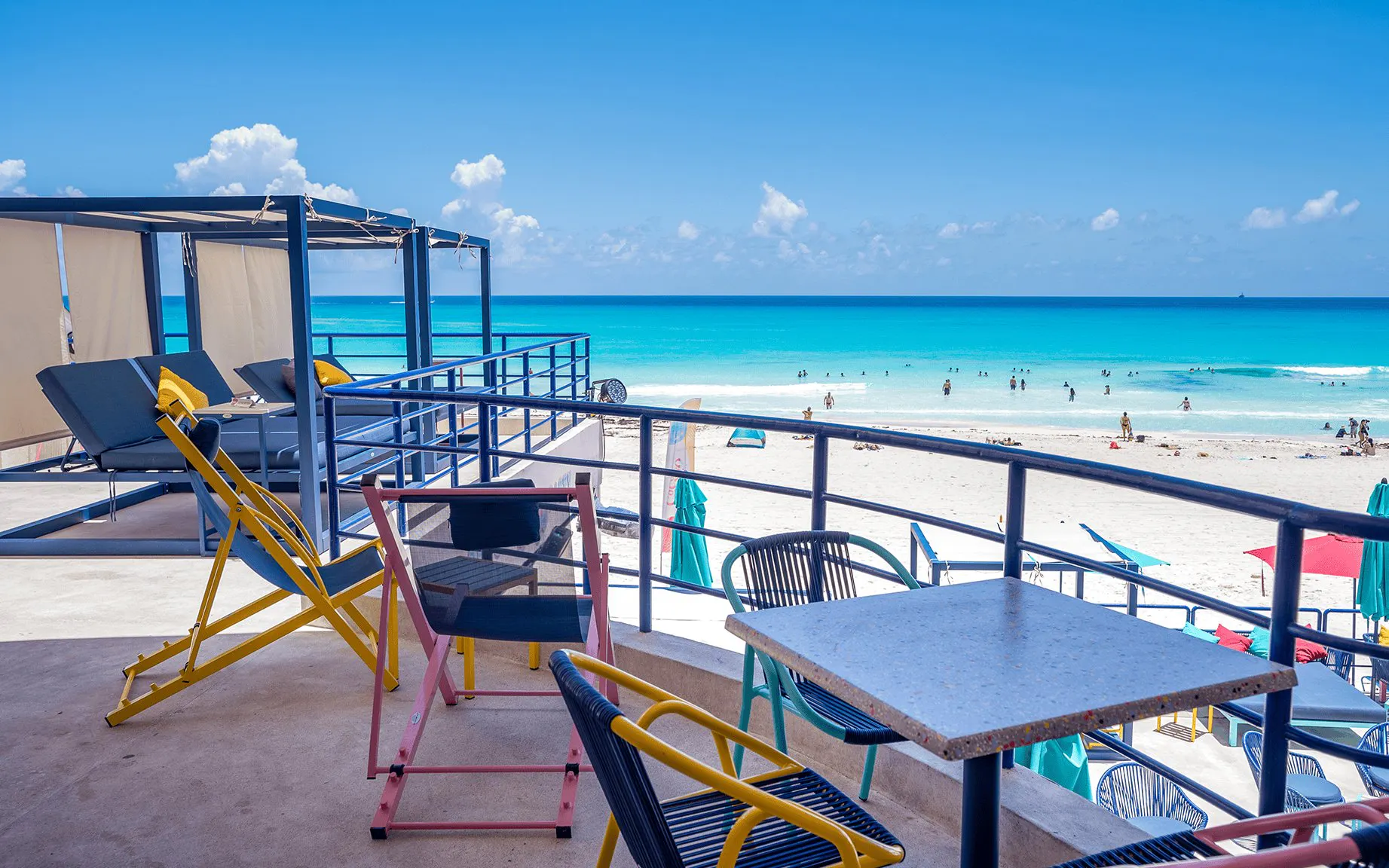 Outdoor seating overlooking Coco Bongo Beach with turquoise water and people swimming.