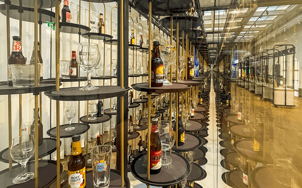 Beer bottles and glasses displayed on shelves at Belgian Beer World Experience.