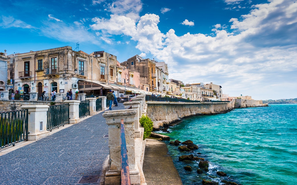 Seaside promenade in Siracusa with historic buildings and ocean view.