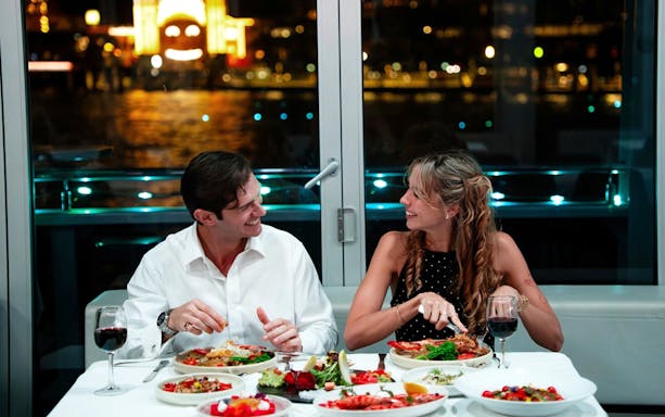 Couple dining on a glass boat cruise in Sydney with city lights in the background.