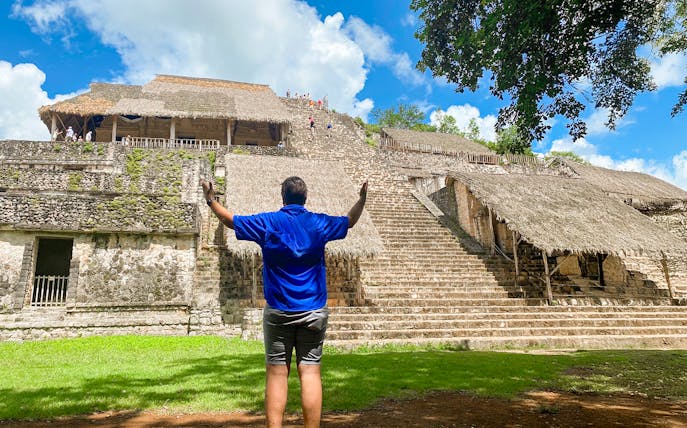 Visitor at Ek Balam pyramid with thatched structures and jungle backdrop in Yucatan, Mexico.