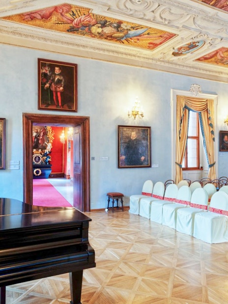 Lobkowicz Palace Museum interior with ornate ceiling, paintings, and seating arrangement.