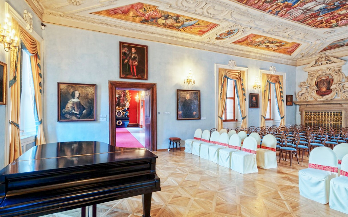 Lobkowicz Palace Museum interior with ornate ceiling, paintings, and seating arrangement.