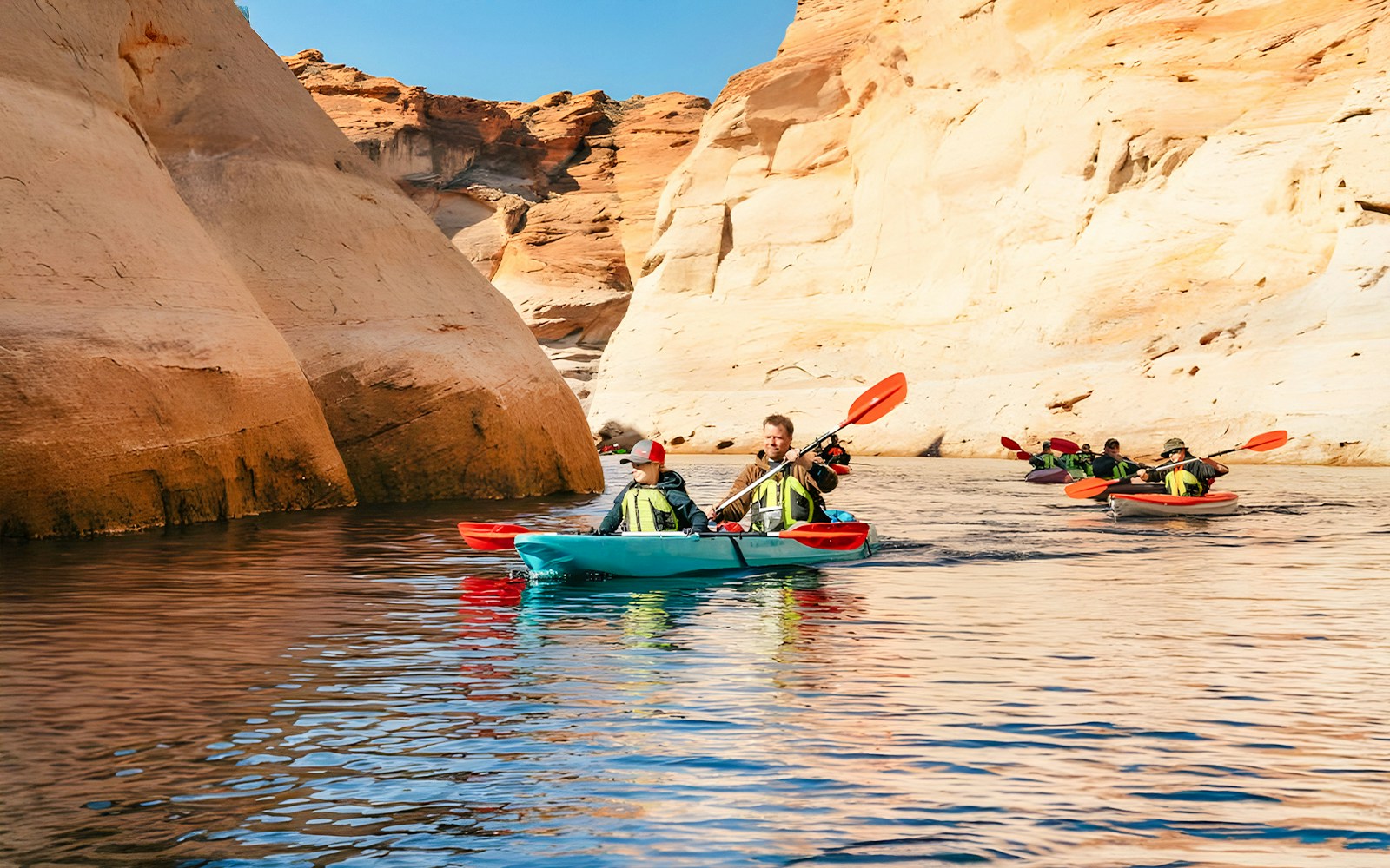 Kayakers paddling on Lake Powell near Antelope Canyon's sandstone cliffs.