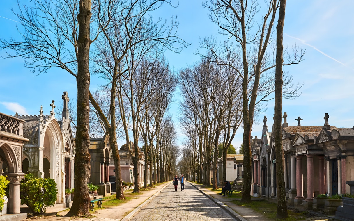 Cobblestone path lined with tombs and trees at Père Lachaise Cemetery, Paris.