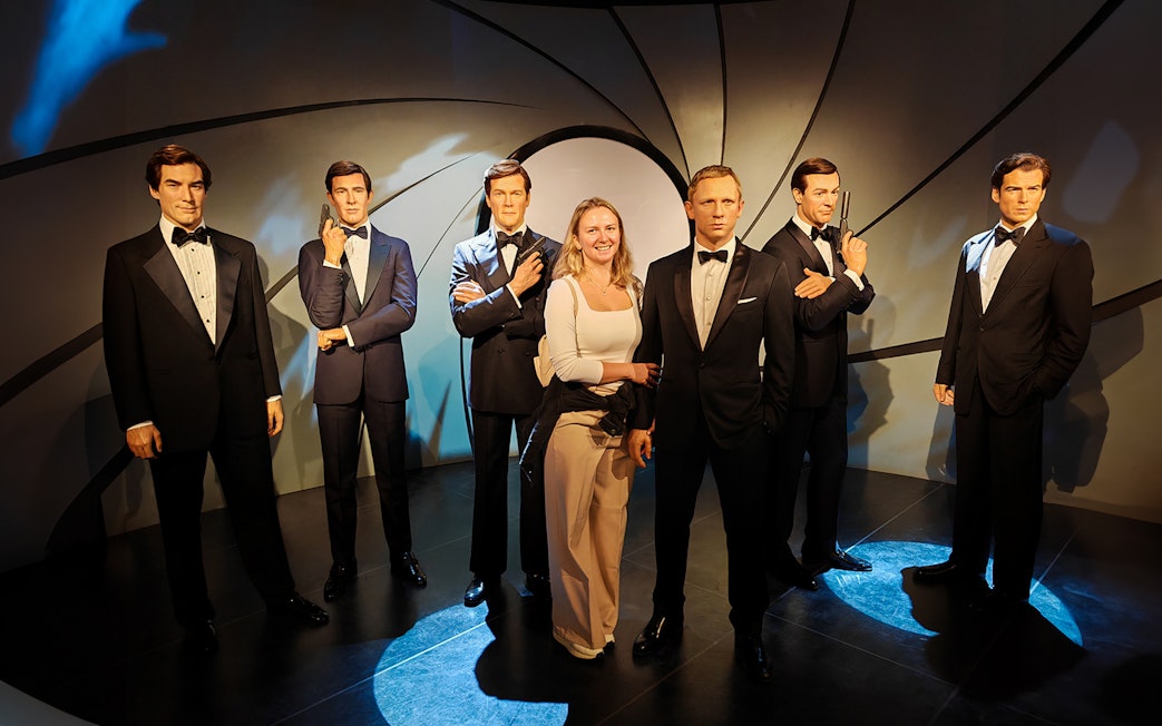 Wax figures of James Bond actors at Madame Tussauds with a visitor.