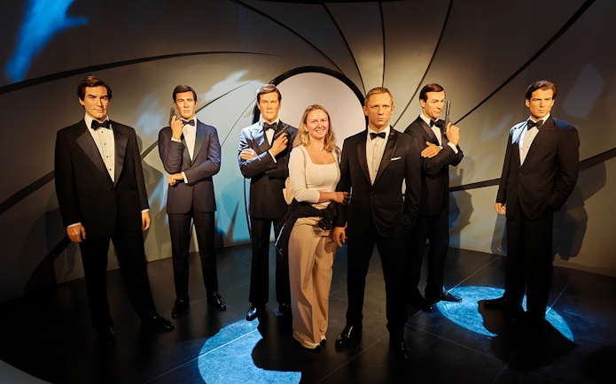 Wax figures of James Bond actors at Madame Tussauds with a visitor.