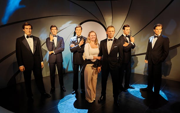 Wax figures of James Bond actors at Madame Tussauds with a visitor.