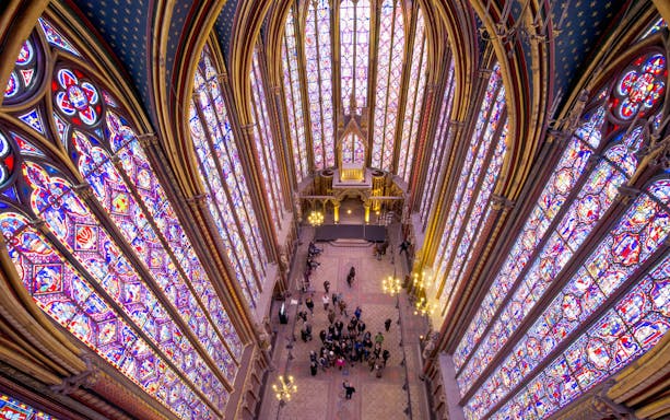 Group tour inside Sainte Chapelle, Paris, with vibrant stained glass windows.