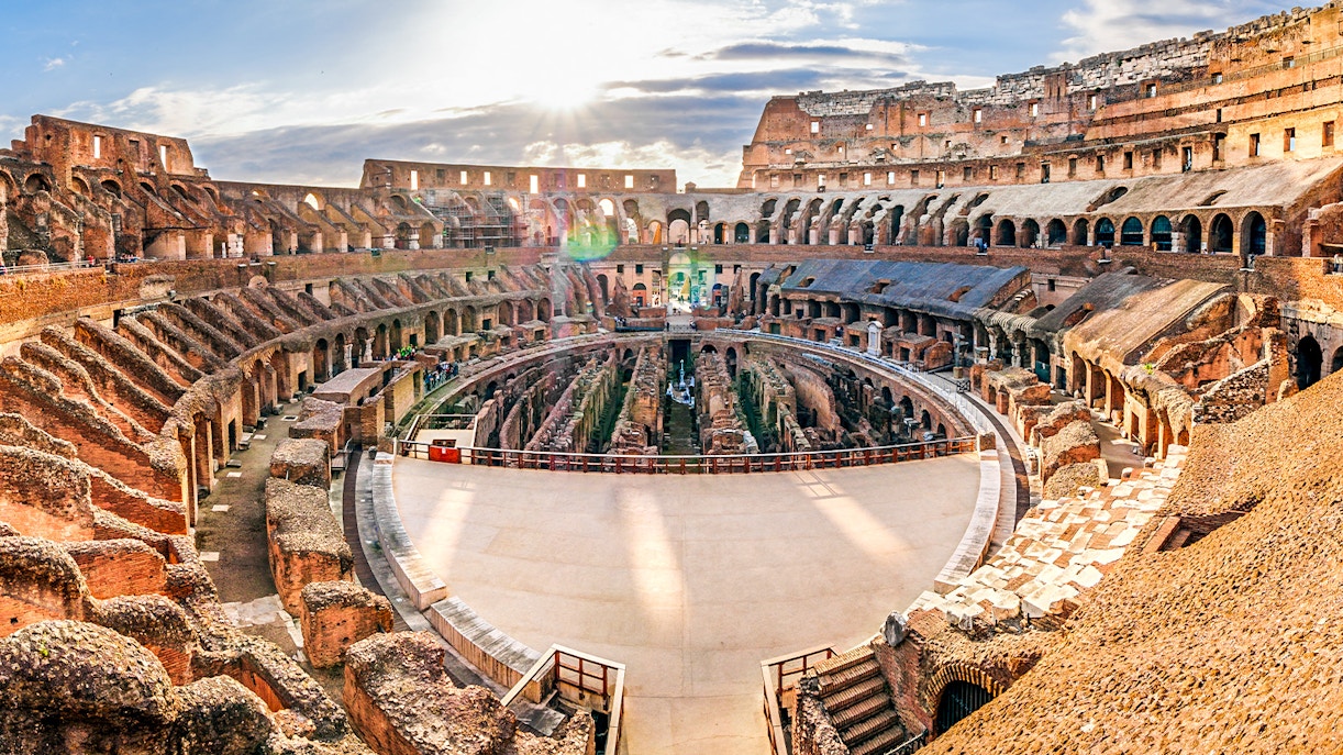 Colosseum arena in Rome with ancient stone seating and sunlight streaming through.