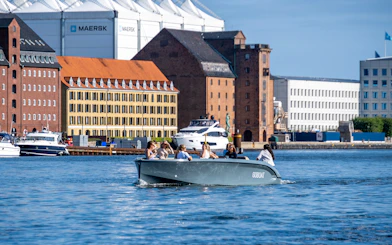 Guests on a boat tour in Copenhagen harbor with historic buildings in the background.