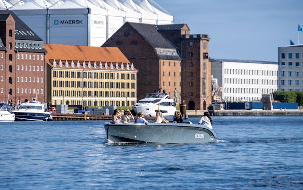 Guests on a boat tour in Copenhagen harbor with historic buildings in the background.