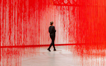 Visitor walking through red string art installation at Kunsthalle Praha.