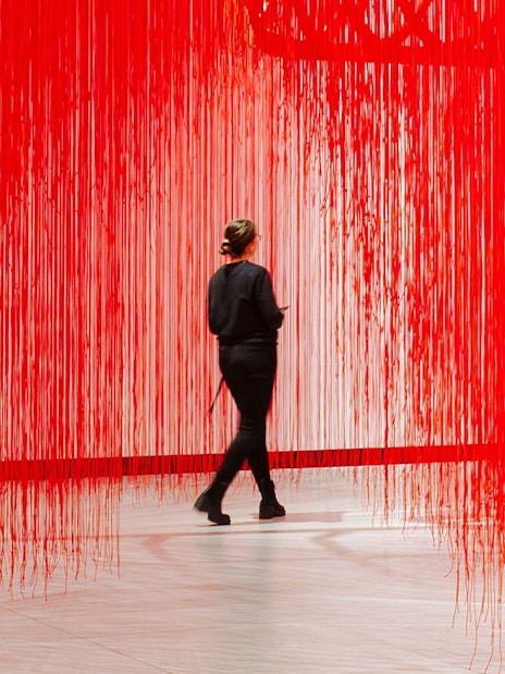 Visitor walking through red string art installation at Kunsthalle Praha.
