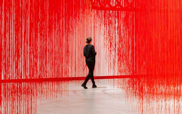 Visitor walking through red string art installation at Kunsthalle Praha.