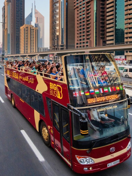 Open-top tour bus on Dubai highway with city skyscrapers in the background.
