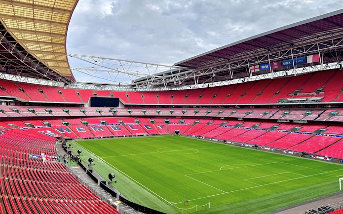 Wembley Stadium interior with empty red seats and green pitch, London.