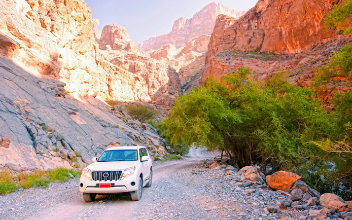 Car on rocky path in oasis surrounded by mountains, Oman.
