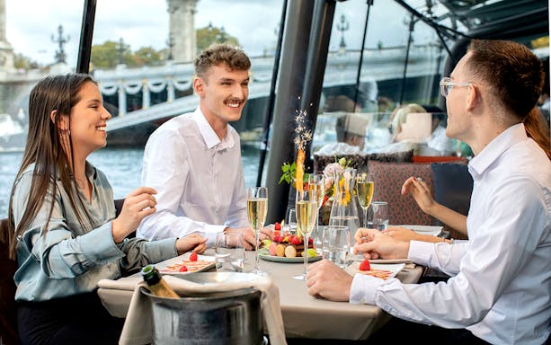 Guests enjoying a festive meal on a Paris Christmas cruise with Eiffel Tower views.