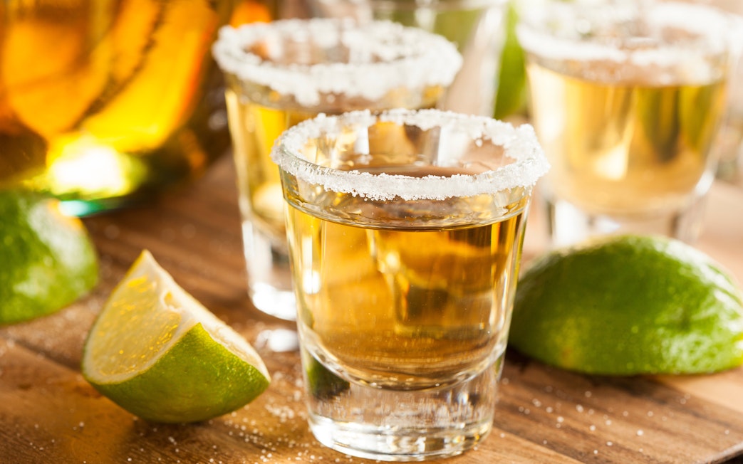 Tequila shots with salt rim and lime wedges on a wooden table.