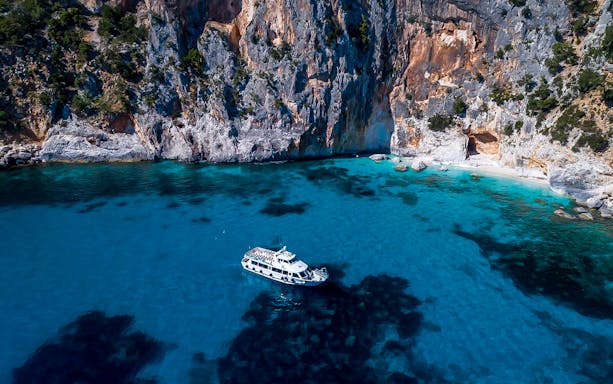 Cruise boat on turquoise waters near rocky cliffs in Gulf of Orosei, Cala Gonone.