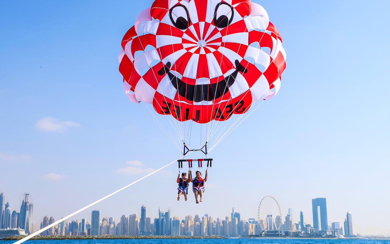 Parasailing over Dubai skyline with colorful parachute.