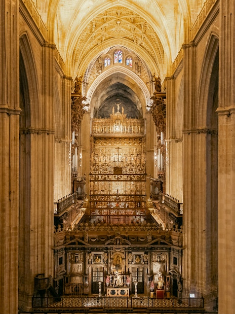 Seville Cathedral interior with ornate altar and vaulted ceilings.