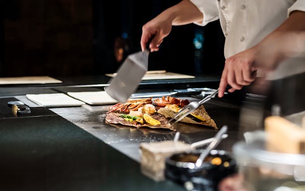 Chef preparing food on a Teppanyaki grill with spatulas.