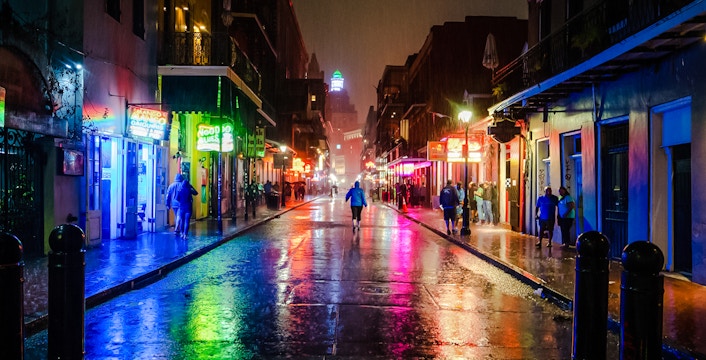 Bourbon Street at night with neon lights reflecting on wet pavement, New Orleans.