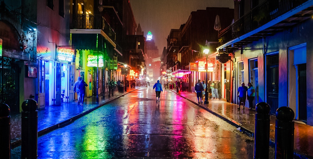 Bourbon Street at night with neon lights reflecting on wet pavement, New Orleans.