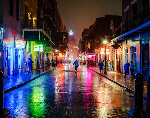 Bourbon Street at night with neon lights reflecting on wet pavement, New Orleans.
